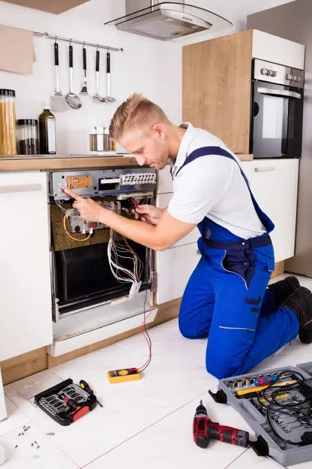 Technician kneeling beside a dishwasher while checking its control wiring
