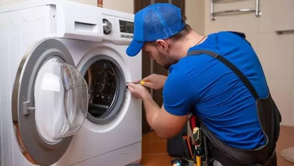 Blue-uniformed technician repairing an open front-loading washing machine